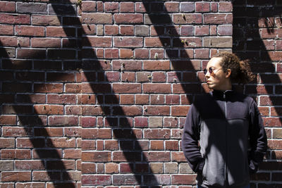 Young man looking away against brick wall