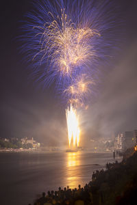 Firework display over sea against sky at night