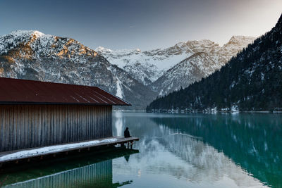 Rear view of man sitting on pier over lake during winter