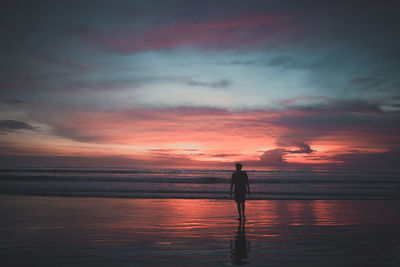 Silhouette man standing at beach against dramatic sky during sunset
