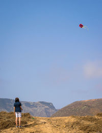 Rear view of man standing on mountain against sky