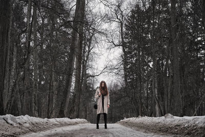 Full length of woman standing on road at forest during winter