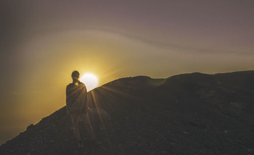Full length of female hiker standing on mountain against sky during sunset