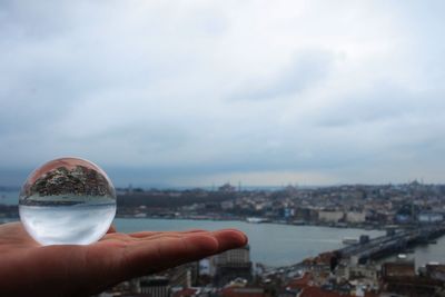 Cropped image of hand holding crystal ball with city in background