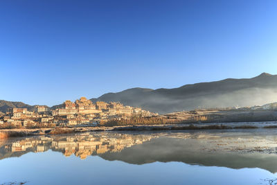 Reflection of ganden sumtseling monastery on lake against clear blue sky