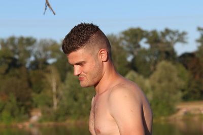 Side view of shirtless man standing against trees in forest