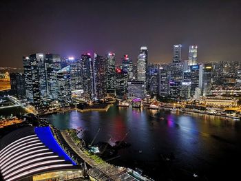 Illuminated buildings by river against sky in city at night