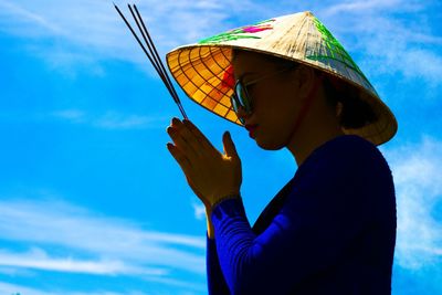 Woman praying while wearing hat against blue sky