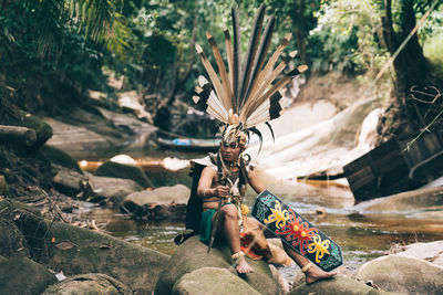 Mid adult man sitting on rock wearing costume by river in forest