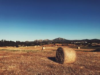 Hay bales on field against clear blue sky