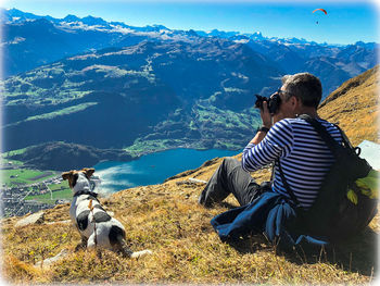 Rear view of man and dog sitting on mountain against sky