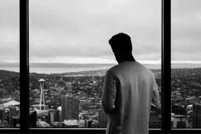 Rear view of man looking at space needle from window of columbia center in city