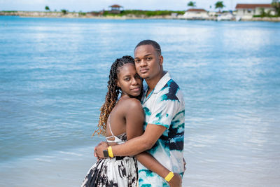 Portrait of a young smiling couple standing on the beach against the sea