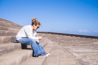 Woman sitting on steps against blue sky