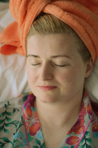 Young woman in orange towel on her head after bath doing self-care procedures at home