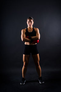 Full length of young woman standing against black background