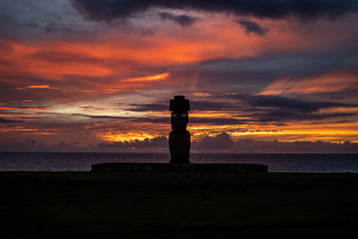 Silhouette cross on beach against sky during sunset