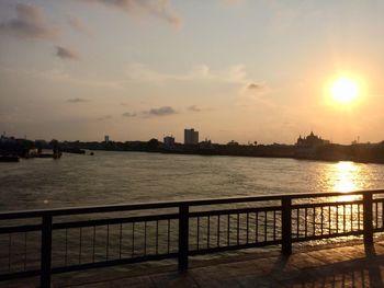 Scenic view of river by buildings against sky during sunset