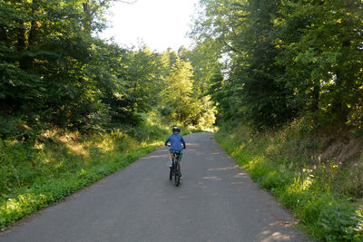 Rear view of boy riding bicycle on road