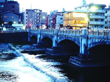 Bridge over river against illuminated buildings in city