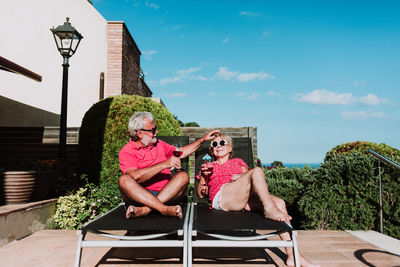 High angle of relaxed senior couple lying on loungers on terrace and drinking refreshing tropical cocktails while enjoying summer holiday