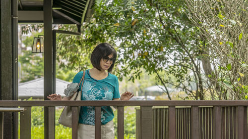 Girl standing by railing against trees