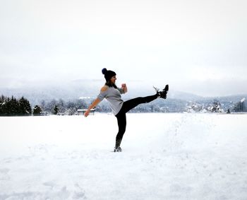 Full length of woman kicking in snow against sky