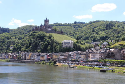 View of town by river against cloudy sky