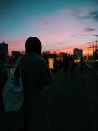 Rear view of silhouette man standing on street against sky during sunset