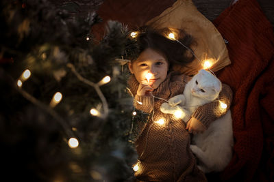 Cozy girl and domestic cat are under the christmas tree, dark golden style. 