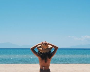 Rear view of young woman wearing sun hat on beach against clear sky