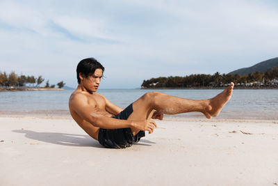 Portrait of shirtless man sitting on beach against sky