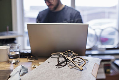 Midsection of male owner using laptop at desk in eyeglasses workshop