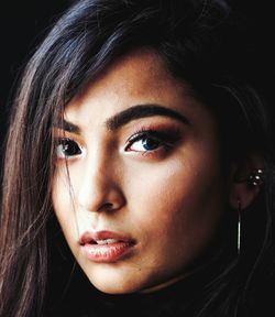 Close-up portrait of beautiful young woman against black background