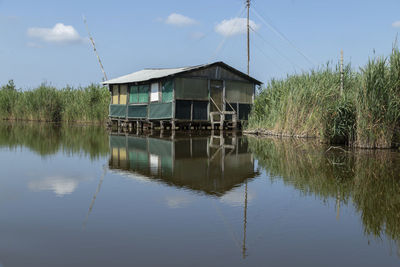 Built structure by lake and still house boat against sky