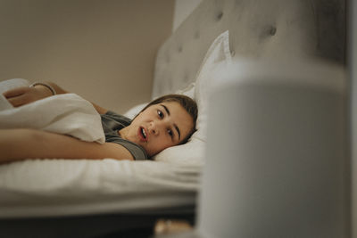 Pre-adolescent girl resting on bed in bedroom at modern home