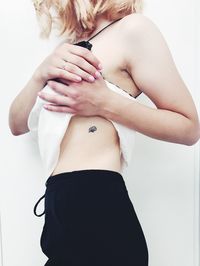 Midsection of woman with tattoo on stomach over white background