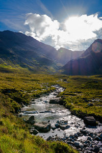 Stream flowing through mountains against sky