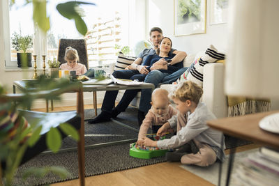Kids playing with parents relaxing on sofa at home