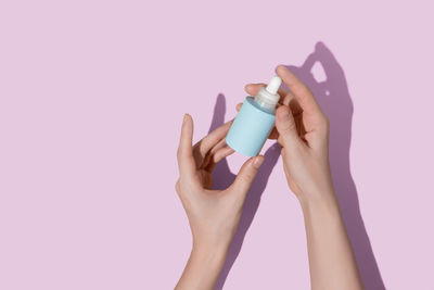 Woman's hands holding blue bottle of cosmetic serum on pink background. high quality photo