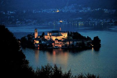 Illuminated cityscape by river against sky at night