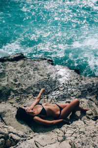 High angle view of woman wearing bikini lying on rock at beach