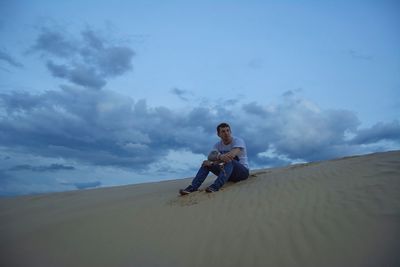Man sitting on sand at beach against sky