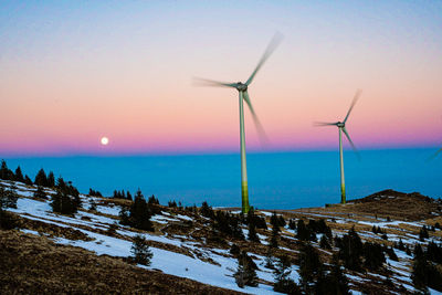 Wind turbines on landscape against sky during sunset