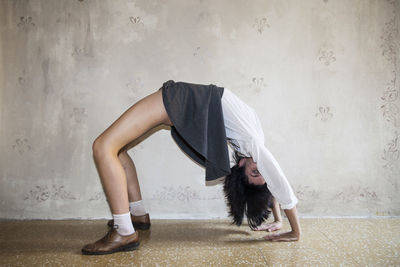 Full length of woman practicing yoga against wall