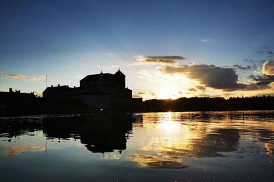 Silhouette buildings by lake against sky during sunset