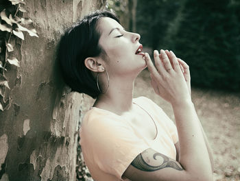 Woman with eyes closed leaning on tree trunk