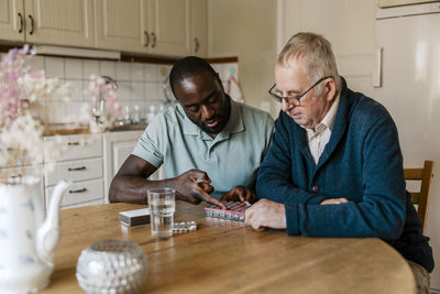 Male nurse explaining medication dosage to senior man sitting at table in kitchen