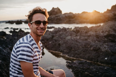 Portrait of young man wearing sunglasses standing at beach