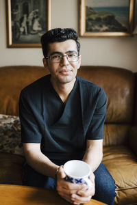 Portrait of smiling male caregiver with coffee cup in living room at home